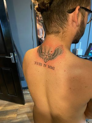 Small lettering diamond and roman numerals tattoo on upper back by Frankie Brown. Black and gray style.