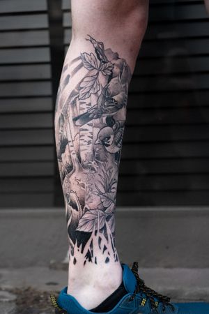 Elegant lower leg tattoo of a bird surrounded by delicate leaves, expertly done by Luca Salzano.