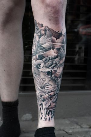 Stunning black and gray lower leg tattoo featuring a detailed micro realism bird, tree, and plants motif by Luca Salzano.