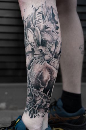 Get inked with a stunning black and gray tattoo of a rabbit and tree on your lower leg by tattoo artist Luca Salzano.