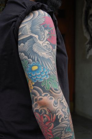 A stunning sleeve tattoo featuring a Japanese inspired design of a bird surrounded by delicate flowers, created by talented artist Bananajims.