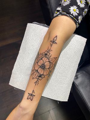 Beautiful fine line tattoo featuring a delicate flower and arrow design by Joanna Webb, with intricate line work.