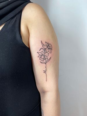 A delicate upper arm tattoo combining fine dotwork, small lettering, and floral motifs with a meaningful quote and leaf accents by talented artist Joanna Webb.