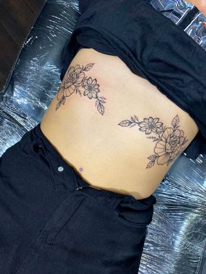 Elegant fine line tattoo featuring intricate flowers and plants on the ribs, expertly done by Joanna Webb.