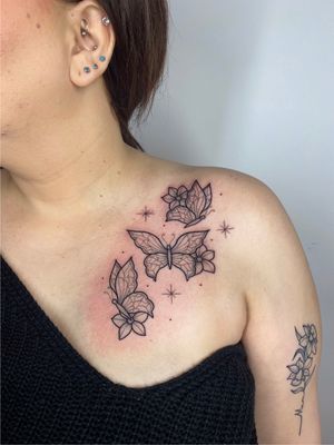 Elegant and delicate chest tattoo of butterfly and flowers by Joanna Webb, showcasing intricate fine line work.