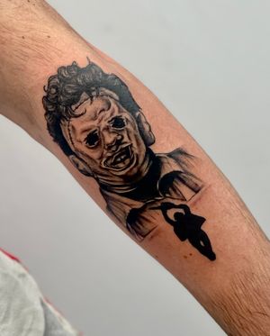 Forearm tattoo by Miss Vampira featuring a detailed blackwork design of Leatherface's iconic mask.