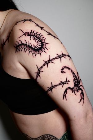 Unique upper arm tattoo featuring a sinister centipede crawling through barbed wire, created by Miss Vampira. Bold and edgy blackwork design.