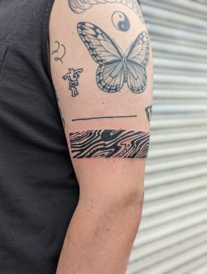 Experience the magic of fine line surrealism with this exquisite black and gray butterfly and pattern upper arm tattoo by artist George Antony.