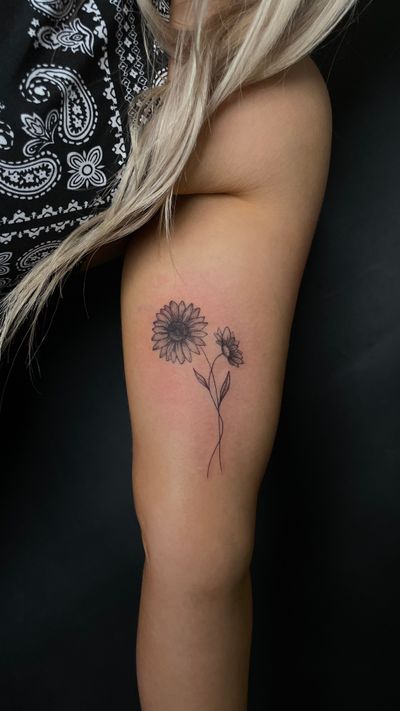 Elegant floral design of a sunflower on upper arm, beautifully executed in fine line style by Kiky Flore.