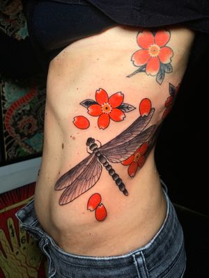 Experience the elegance of Andrea Furci's intricate Japanese design featuring a dragonfly and flower on the ribs. Enhance your body art with this beautiful and symbolic tattoo.