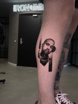 Impressive blackwork portrait of Kanye West on lower leg, skillfully done by artist Artemis.