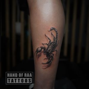 Bold black scorpion design by Raa, perfect for a lower leg statement piece. Embrace your inner strength with this striking tattoo.