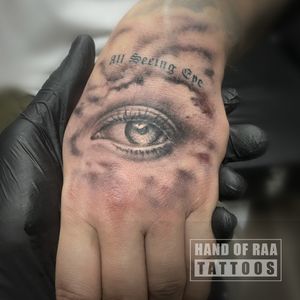 Unique black and gray small lettering tattoo on hand featuring an intricate eye and inspiring quote by artist Raa.