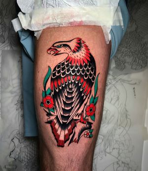 Get a stunning traditional style tattoo featuring an eagle and flower on your upper leg by the talented artist Ryan Goodrum.