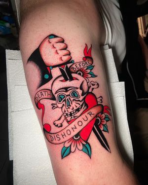 Traditional lettering tattoo on upper arm with a skull motif and inspirational quote, expertly done by artist Ryan Goodrum.