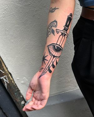 Get inked with a striking blackwork tattoo featuring a sword and eye design by Adrimetric. Perfect for those seeking a bold and illustrative piece.