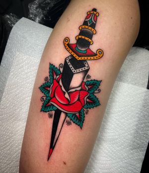Intricate design by Ryan Goodrum featuring a vibrant flower and sharp dagger on the upper arm. A timeless symbol of beauty and strength.