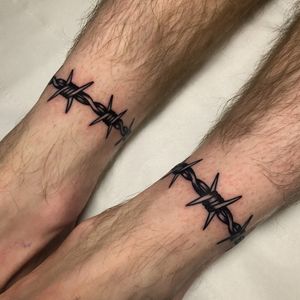 Get edgy with this traditional tattoo featuring barbed wire and spikes, done by talented artist Ryan Goodrum on the lower leg.