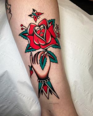 Vibrant traditional tattoo on lower leg, featuring a beautiful flower and hand design by artist Ryan Goodrum.