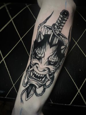 Blackwork tattoo by Kike Krebs featuring a Japanese sword and fierce Hannya mask motif on the forearm.