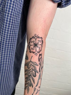 Adorn your arm with a delicate design of flowers, leaves, and ornamental elements by the talented artist Jack Henry.