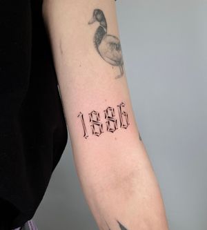 Joshua Williams beautifully combines black and gray realism with elegant lettering to commemorate the year 1992 on your arm.