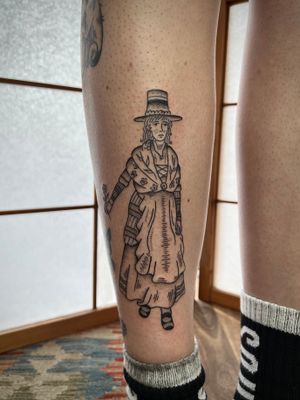 Elegant black and gray tattoo of a woman wearing a stylish hat on the shin, done by Jack Henry Tattoo.