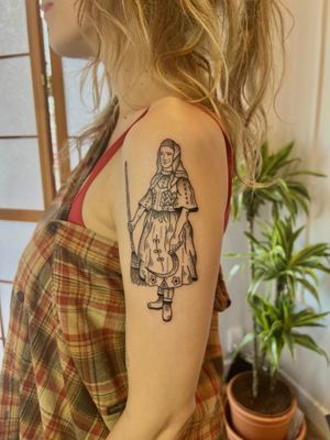 Elegant black and gray fine line tattoo of a lady with a broom on the upper arm, beautifully crafted by Jack Henry.