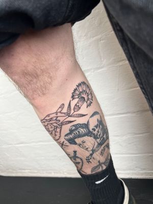 Elegant black and gray tattoo featuring a delicate flower, hand, and leaf by Jack Henry Tattoo on the lower leg.