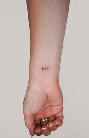 Fine line and small lettering forearm tattoo featuring a simple number design created by artist Gabriele Edu.