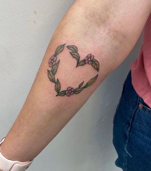 Bright and vibrant new school style tattoo featuring a beautiful flower and leaf design on the forearm by Rachel Angharad.