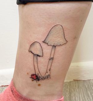 Beautiful lower leg tattoo by Rachel Angharad featuring a delicate mushroom and a charming ladybug design done in fine line style.