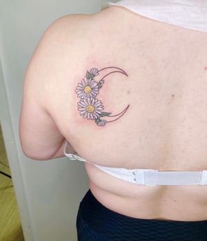 An enchanting floral tattoo featuring a crescent moon and delicate flowers on the upper back by Rachel Angharad.