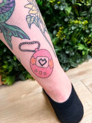 Check out this vibrant lower leg tattoo featuring a heart and tamagotchi, beautifully designed by Rachel Angharad.
