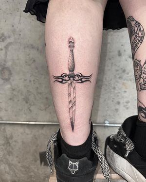 Get a sleek and stylish black and gray dagger tattoo by artist Laura May. Perfect for those looking for a minimalist yet striking piece of body art.