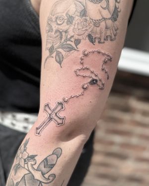 Get a stunning black and gray rosary tattoo with intricate fine line details by the talented artist Laura May.
