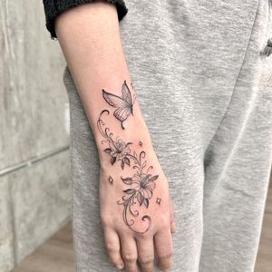 Black and gray fine line butterfly tattoo with intricate floral details by renowned artist Laura May.