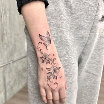 Black and gray fine line butterfly tattoo with intricate floral details by renowned artist Laura May.