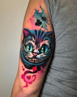 Vibrant new school style upper arm tattoo featuring a whimsical Cheshire Cat surrounded by playing cards. Designed by Cloto.tattoos.