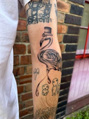 Surreal black and gray tattoo by Jack Howard on arm, featuring a detailed flamingo wearing a hat.