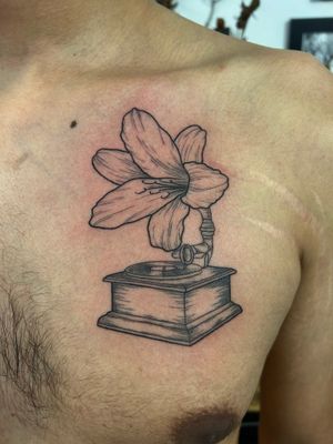 Elegant tattoo by Jack Howard featuring a delicate flower and vintage gramophone design on the chest.