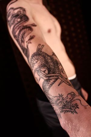 Capture the fierce beauty of a Japanese dragon intertwined with a chain in this striking black and gray lower arm tattoo by skilled artist José.