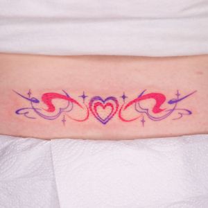 Get a colorful heart tramp stamp tattoo in illustrative tribal style by Mika Tattoos for a unique and bold look.