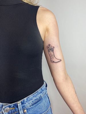 Exquisite upper arm tattoo by Joanna Webb featuring a delicate floral design intertwined with a stylish boot motif.