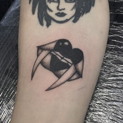 Jenny Dubet's forearm tattoo features a unique blend of blackwork, dotwork, and fine line styles, depicting a heart, vampire, and lips motif symbolizing eternal love.