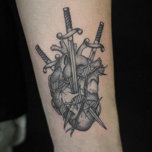 A traditional black and gray tattoo on the forearm by artist Jenny Dubet, featuring a dagger and anatomical heart motif.