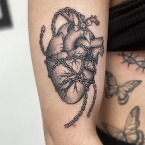 Jenny Dubet's upper arm tattoo combines black and gray, dotwork, and neo-traditional styles to depict a striking anatomical heart design.