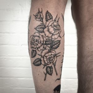 A black and gray neo-traditional tattoo of a beautiful rose entwined with a skull, created by Jenny Dubet. Located on the lower leg.