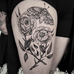 An intricate design featuring a butterfly, flowers, and an eyeball in black and gray, dotwork, and neo-traditional styles by Jenny Dubet. Located on the upper leg.