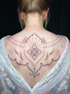Beautiful upper back tattoo featuring intricate dotwork and fine line ornamental design with delicate leaves by Viví Bogdanov.